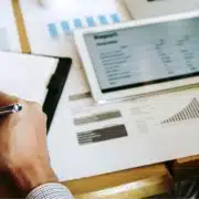 a bookkeeper or accountant recording information in a notebook and discussing graphs and charts with another professional