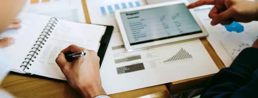 a bookkeeper or accountant recording information in a notebook and discussing graphs and charts with another professional