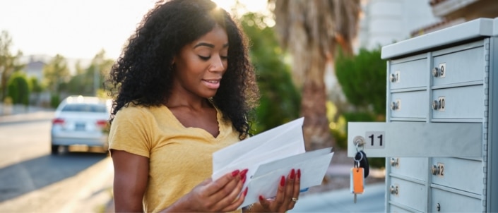 A black woman going through her mail outside of her mailbox