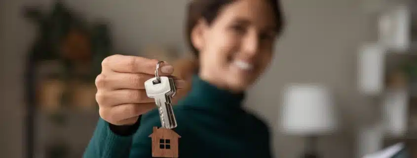 Smiling new homeowner posing by holding out her housekeys in front of her