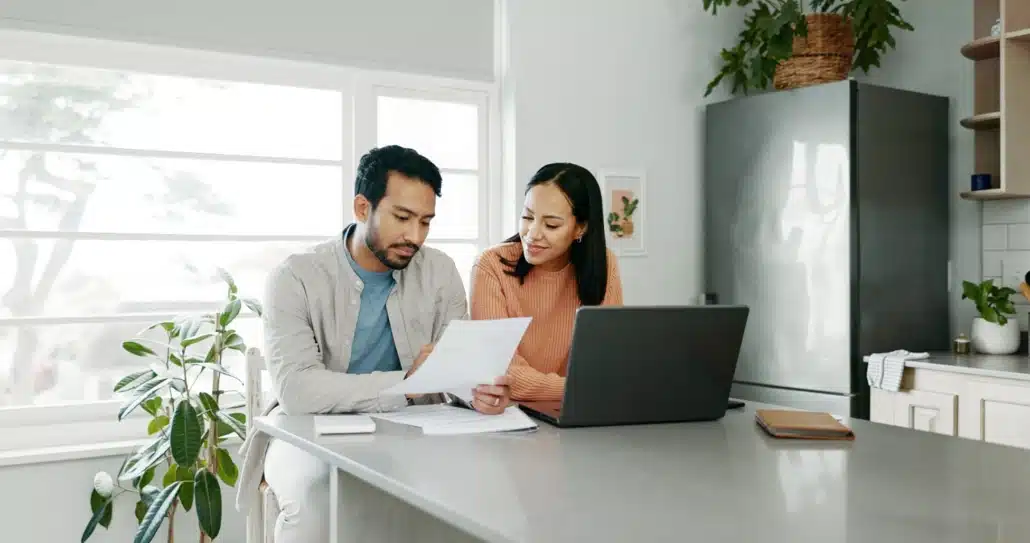 Couple reviewing tax documents and a laptop together at their kitchen counter, discussing back taxes and financial planning at home.