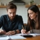 Couple sitting at a table reviewing bills or financial documents together with a laptop and calculator.