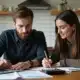 Couple sitting at a table reviewing bills or financial documents together with a laptop and calculator.